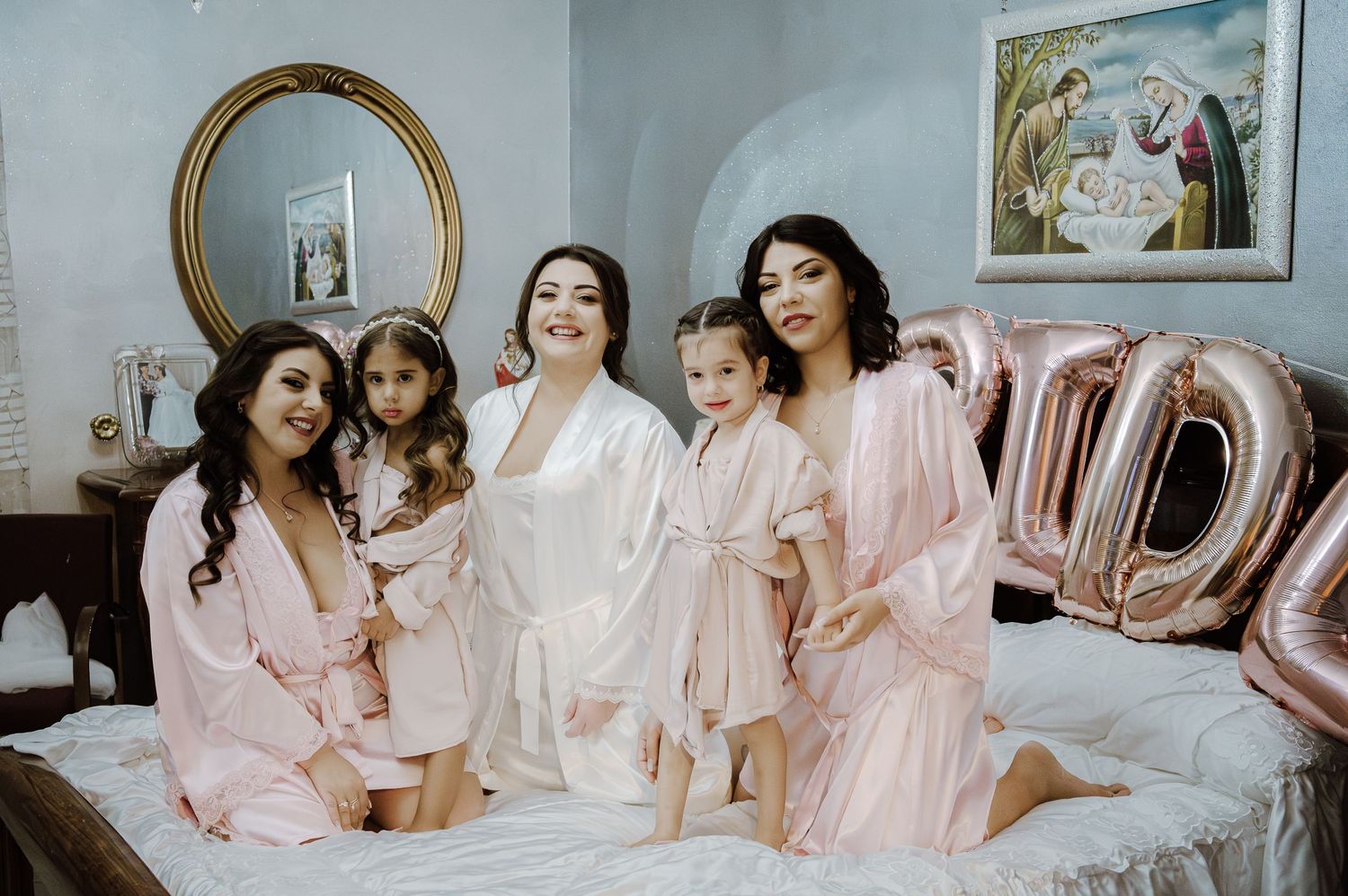 A group wearing matching pink robes pose together on a bed with balloon decorations.