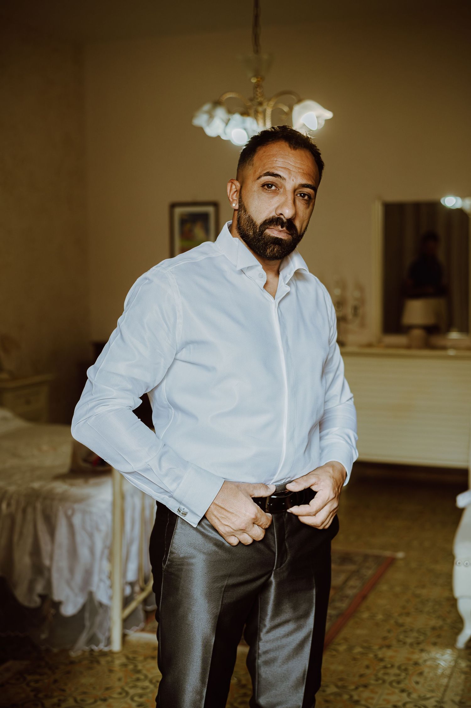Person in white dress shirt and dark pants getting dressed in an elegant indoor setting.