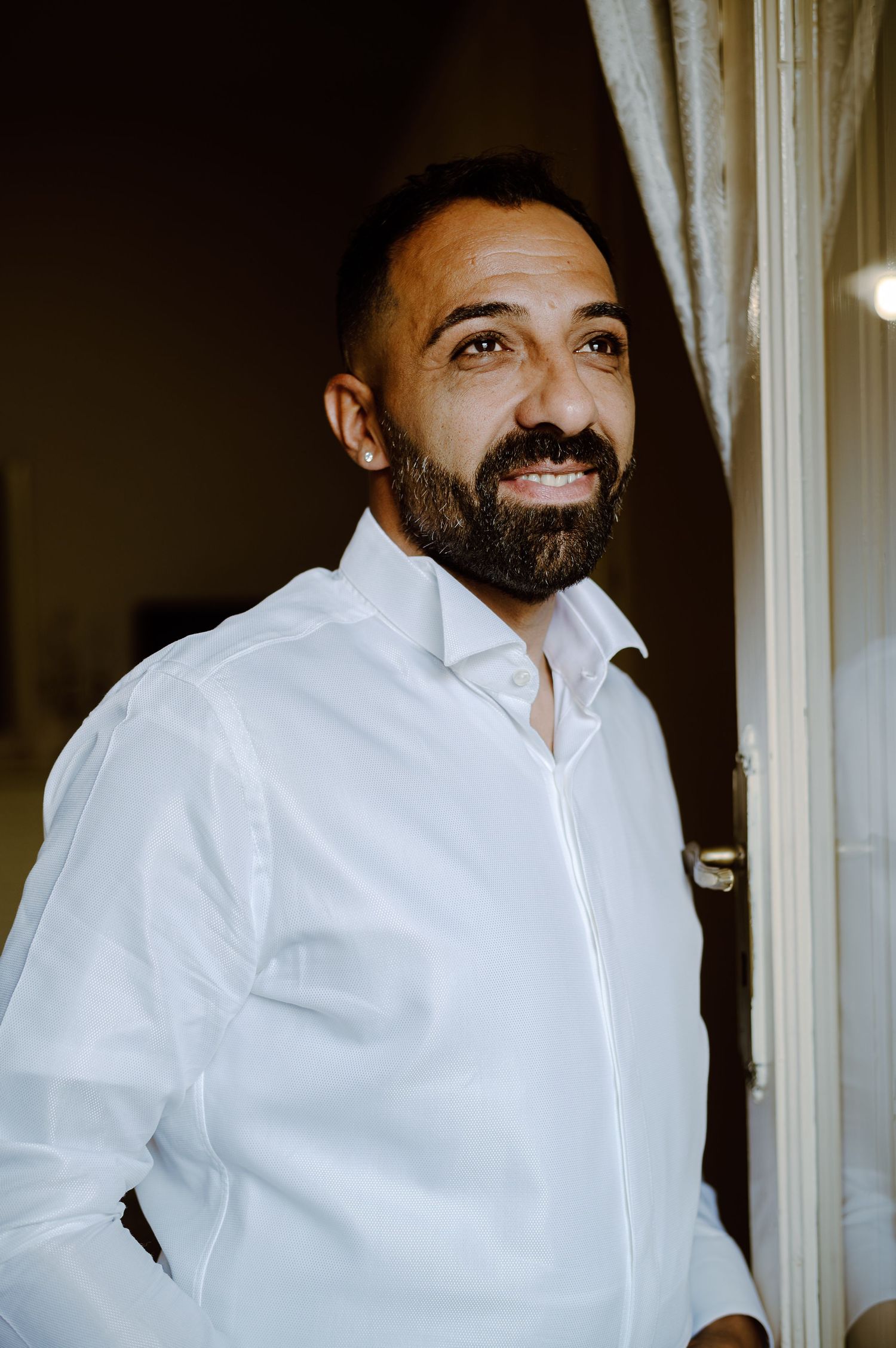 Person wearing a crisp white dress shirt smiling by a window in warm lighting.