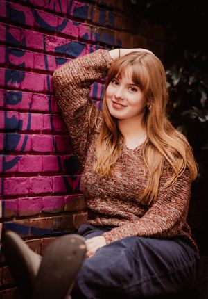 Portrait session against pink brick wall with copper sequined top and dark pants in moody lighting.