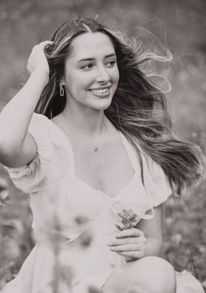 Black and white portrait with flowing hair in light dress holding flower.