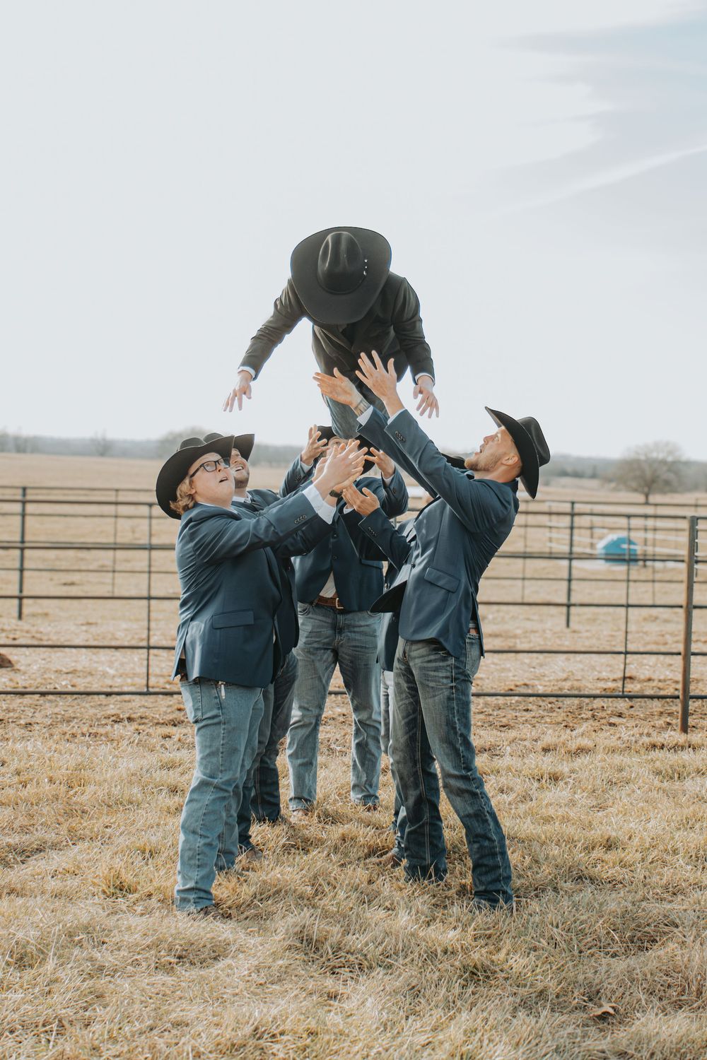 Groomsmen playfully toss someone in the air during outdoor wedding photoshoot.