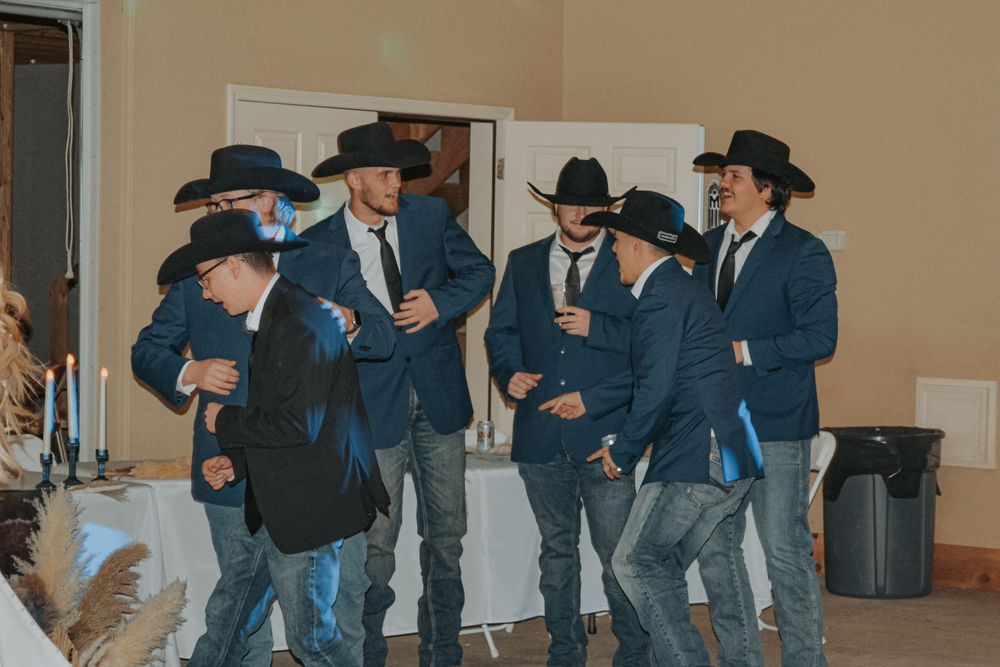 Group of groomsmen in matching navy suits and cowboy hats enjoying the celebration.