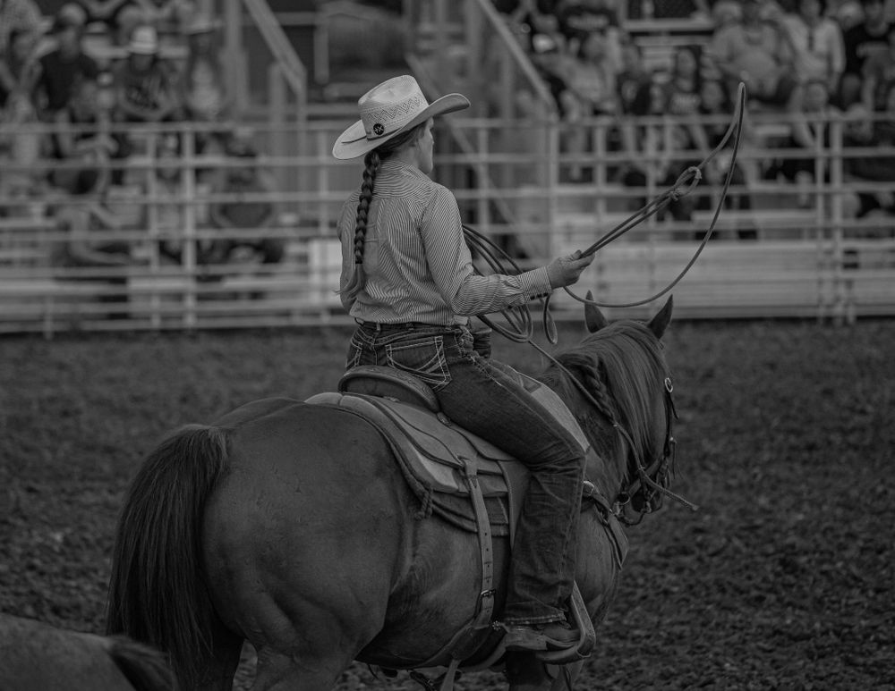 A rodeo competitor sits mounted on horseback in vintage-style black and white photography.