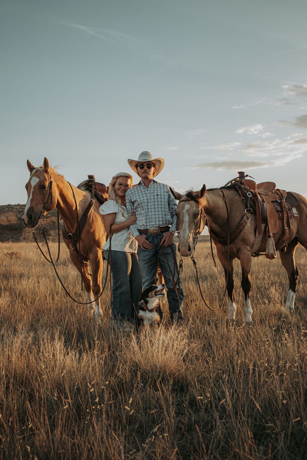 Western couple with horses in rustic prairie setting during golden hour.