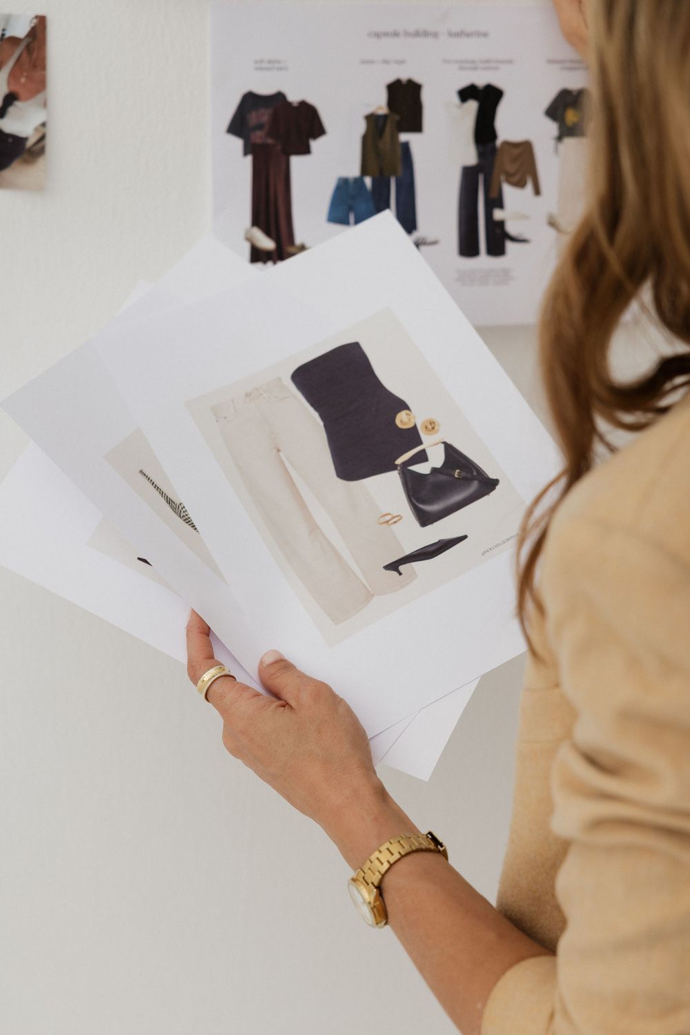 A fashion stylist reviews printed outfit mood boards featuring clothing and accessories in a bright studio.