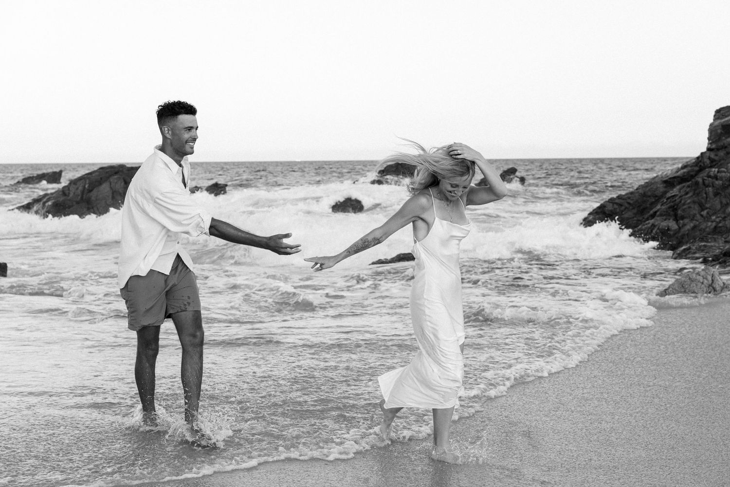 A couple dances together on a beach with crashing waves in the background.