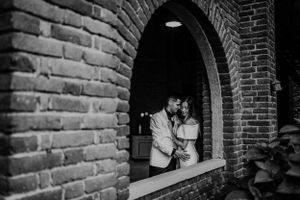 Black and white romantic portrait of a couple embracing inside a brick arched window at night.