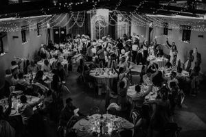 Aerial black and white photo of wedding reception guests seated at round tables in elegant venue with string lights.