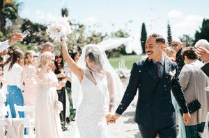 Bride and groom walk down the aisle as guests toss confetti at outdoor wedding ceremony.