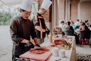Chef in white hat carving roasted meat at outdoor wedding catering station for guests.