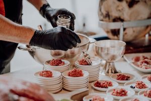 Catering staff in black gloves plating ground meat appetizers on white dishes at wedding reception.