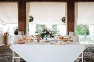 Elegant white dessert table with floral centerpiece under tent at wedding reception.