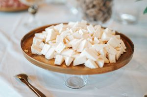 White meringue pieces displayed on wooden pedestal cake stand at wedding dessert table.