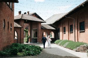 Wedding couple walks hand-in-hand between rustic brick buildings at charming venue.