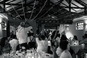 Black and white photo of wedding guests celebrating inside a rustic venue adorned with fairy lights.