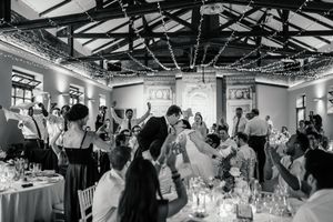 Black and white wedding reception photo with couple dancing surrounded by cheering guests under fairy lights.
