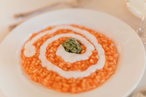 Elegant tomato risotto plated with cream swirl and fresh pesto garnish on a white plate.