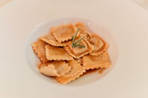 Homemade ravioli pasta served in a white bowl garnished with a fresh rosemary sprig.