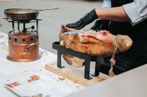 Chef in black gloves carves a whole roasted ham at outdoor wedding catering station.