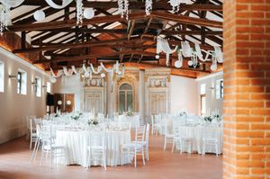Elegant wedding reception hall with white round tables, chiavari chairs, and brick walls.