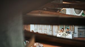 Couple sits intimately together viewed through wooden slats at elegant wedding reception venue.