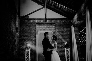 Black and white wedding portrait of bride and groom sharing an intimate moment under dramatic stage lighting.