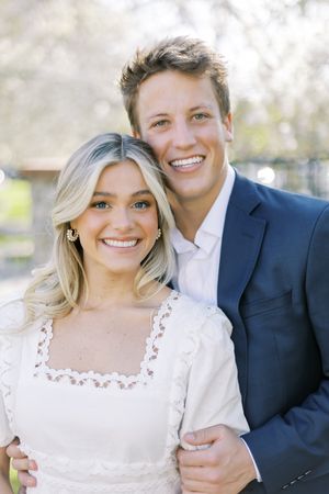 Couple smiling at camera wearing formal attire with white dress and navy suit.