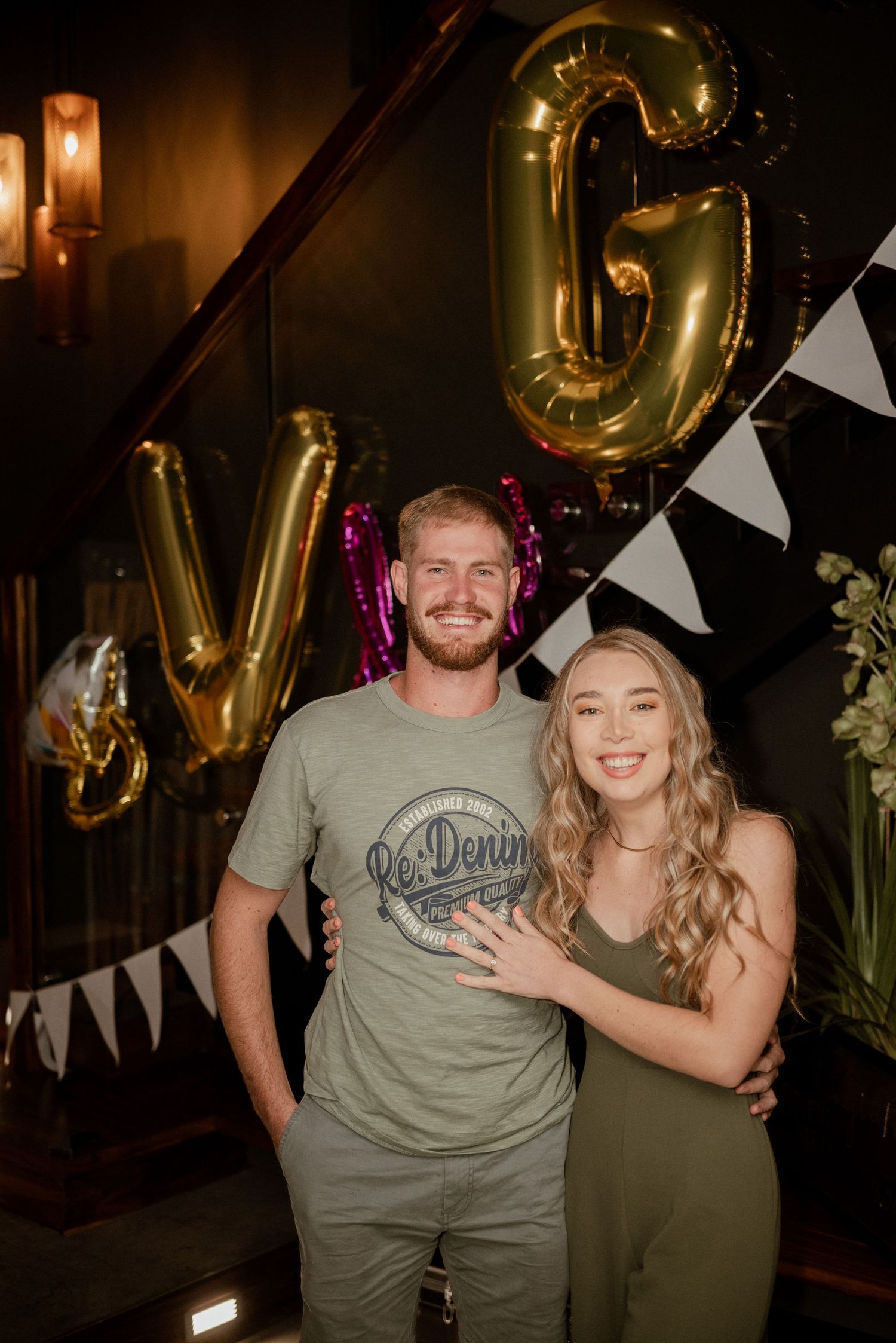 Gold balloon letters and white banner decorations adorn a dark interior party space.