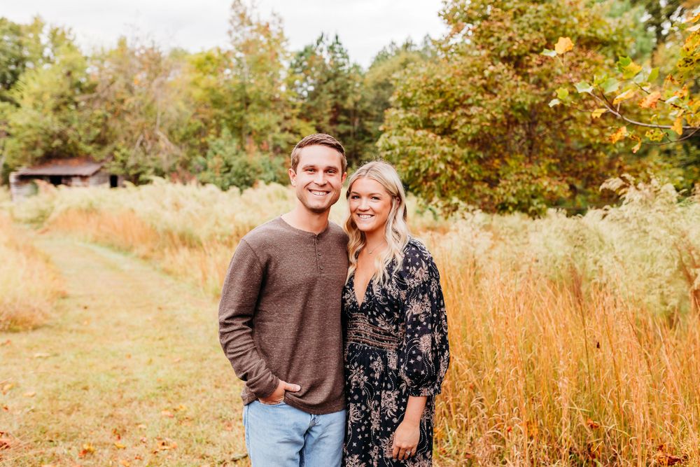 A couple poses together in a golden autumn field during sunset for romantic outdoor portraits.