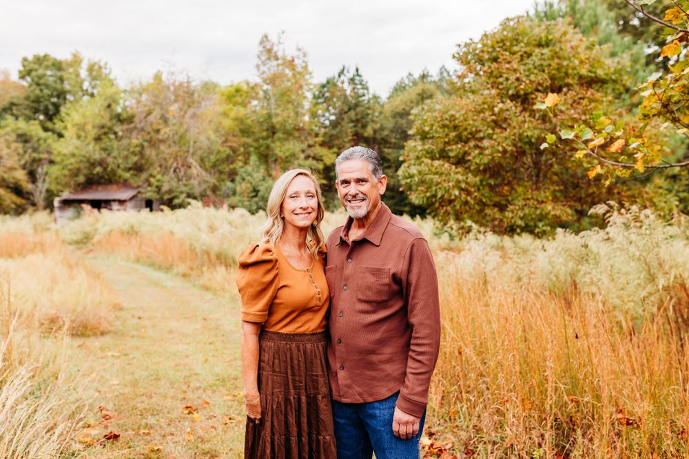 A couple embraces in a golden autumn field with tall grass and trees during a fall photo session.