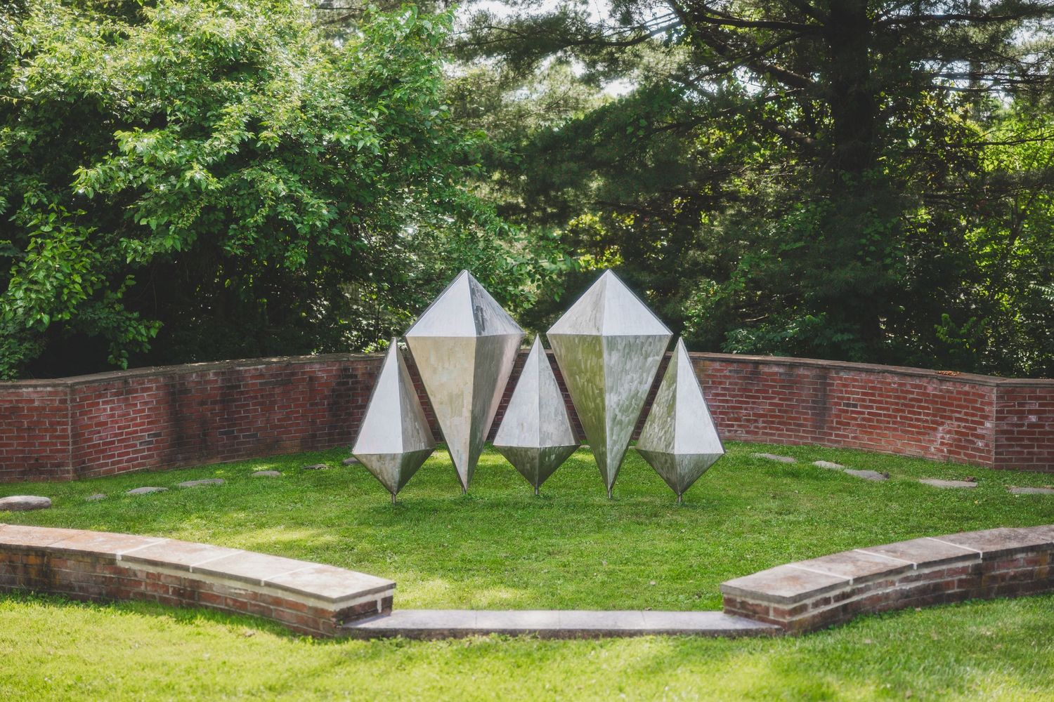 Three modern geometric tent structures arranged on a grassy lawn surrounded by brick walls.