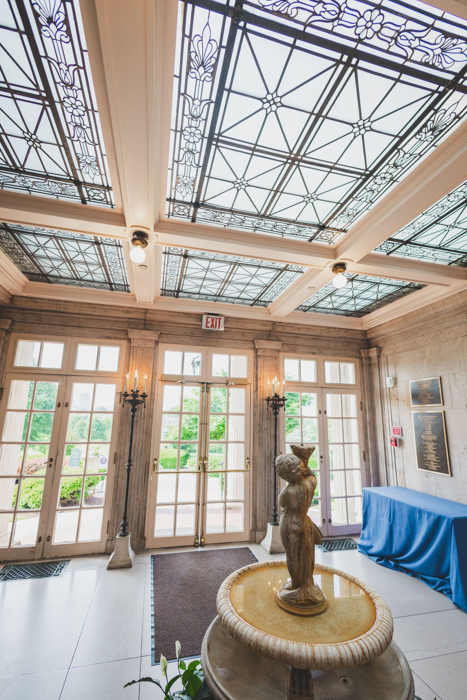 Ornate glass ceiling with intricate metalwork design illuminates a grand interior space with statue fountain.