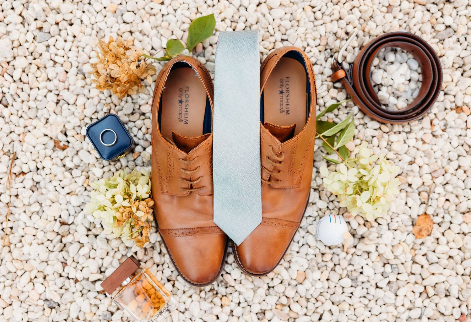 Leather oxford shoes arranged in a row on a speckled stone surface with scattered autumn leaves and decorative elements.