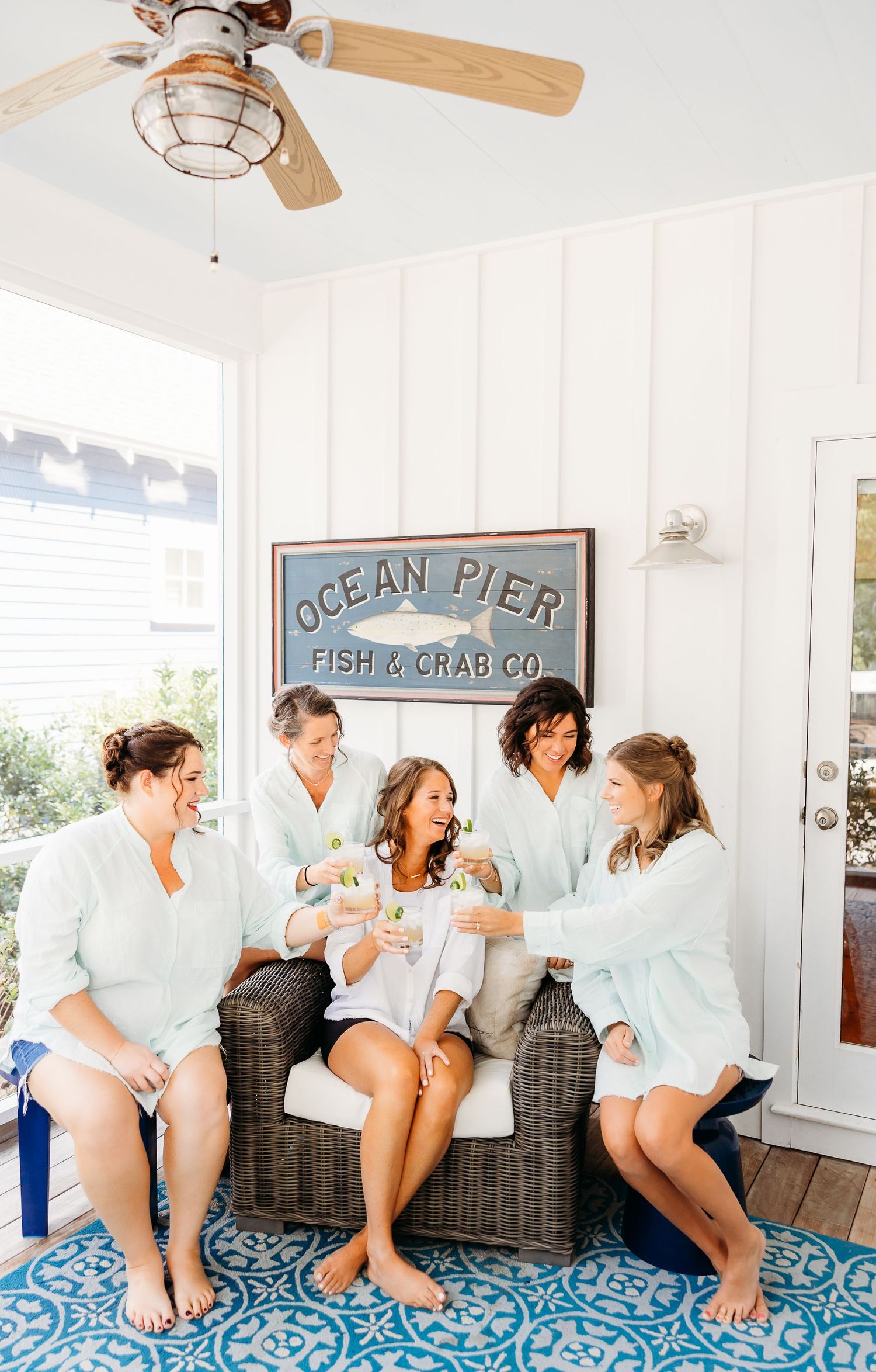 A group in matching white robes sits and laughs together on a blue patterned bench under nautical wall decor.