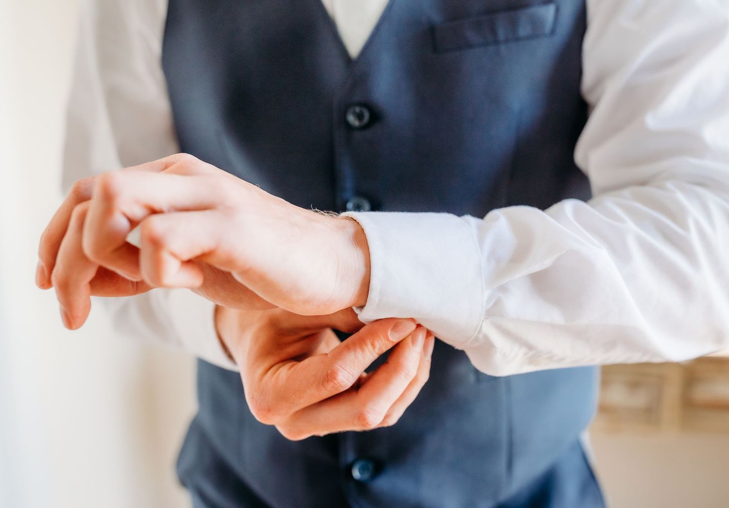Close up view of hands adjusting a navy blue suit vest with matching buttons.