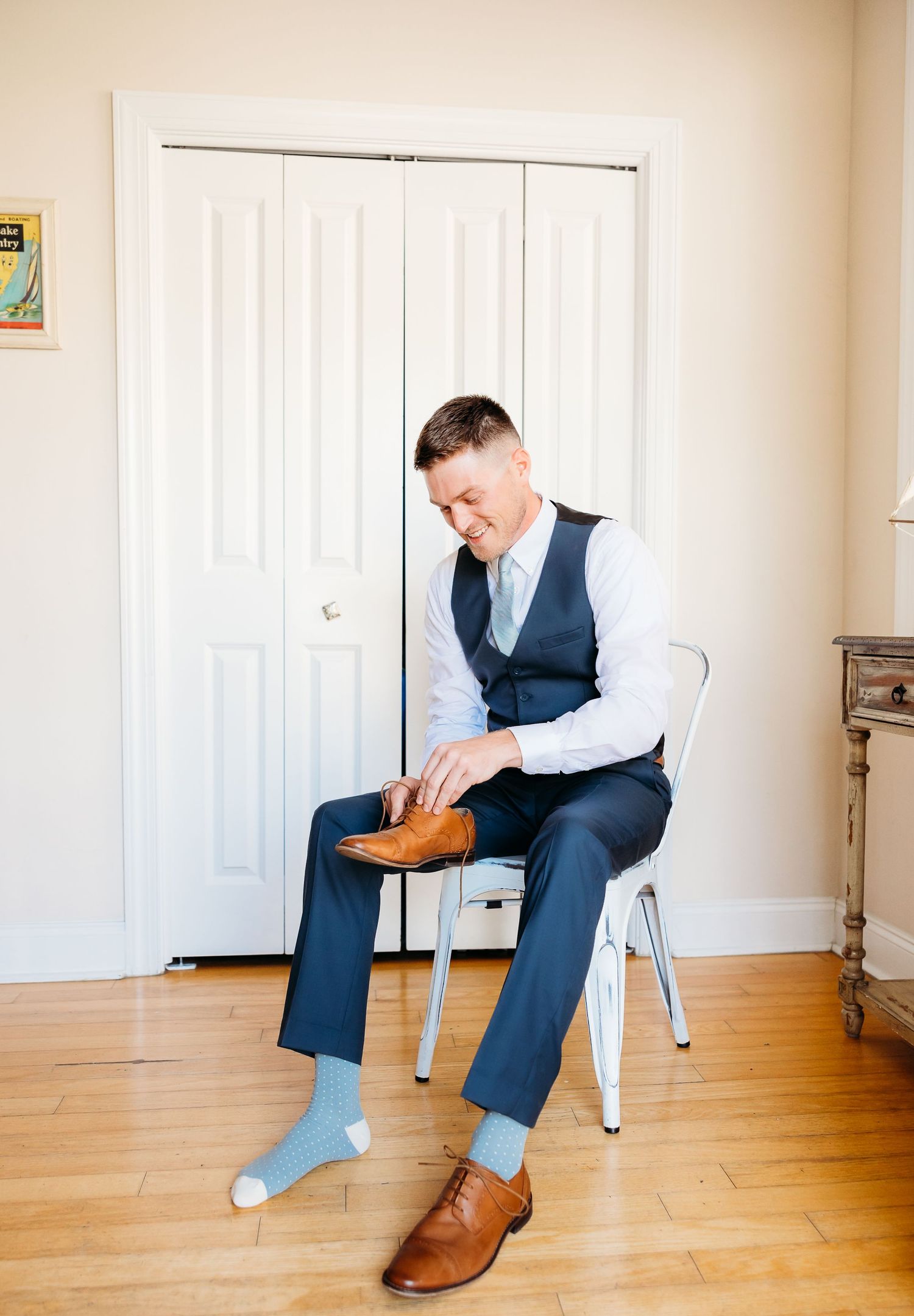 A person in business attire sits on a white chair in a room with hardwood floors and white walls.