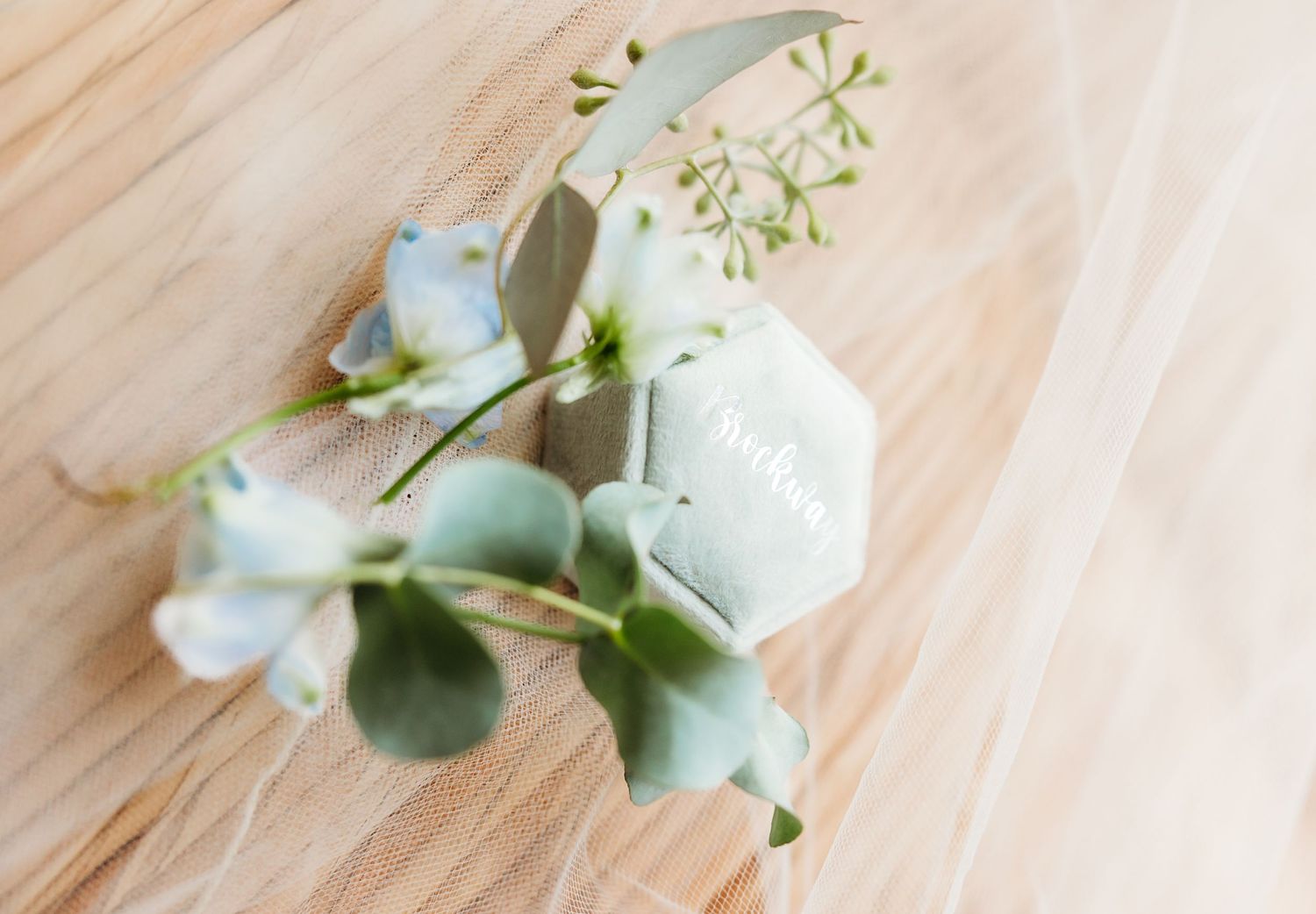 White rose petals and eucalyptus leaves arranged on a light wooden surface create a delicate floral composition.