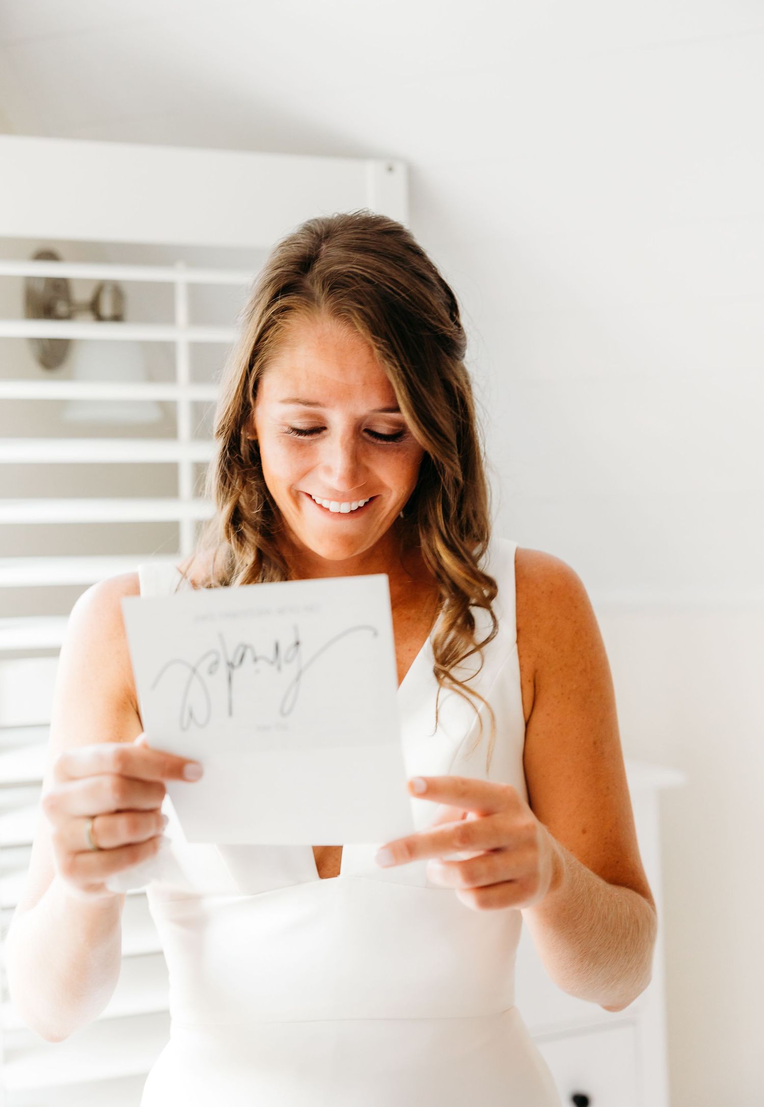 A person in a tan sweater smiles while looking down at handwritten notes in a bright white room.