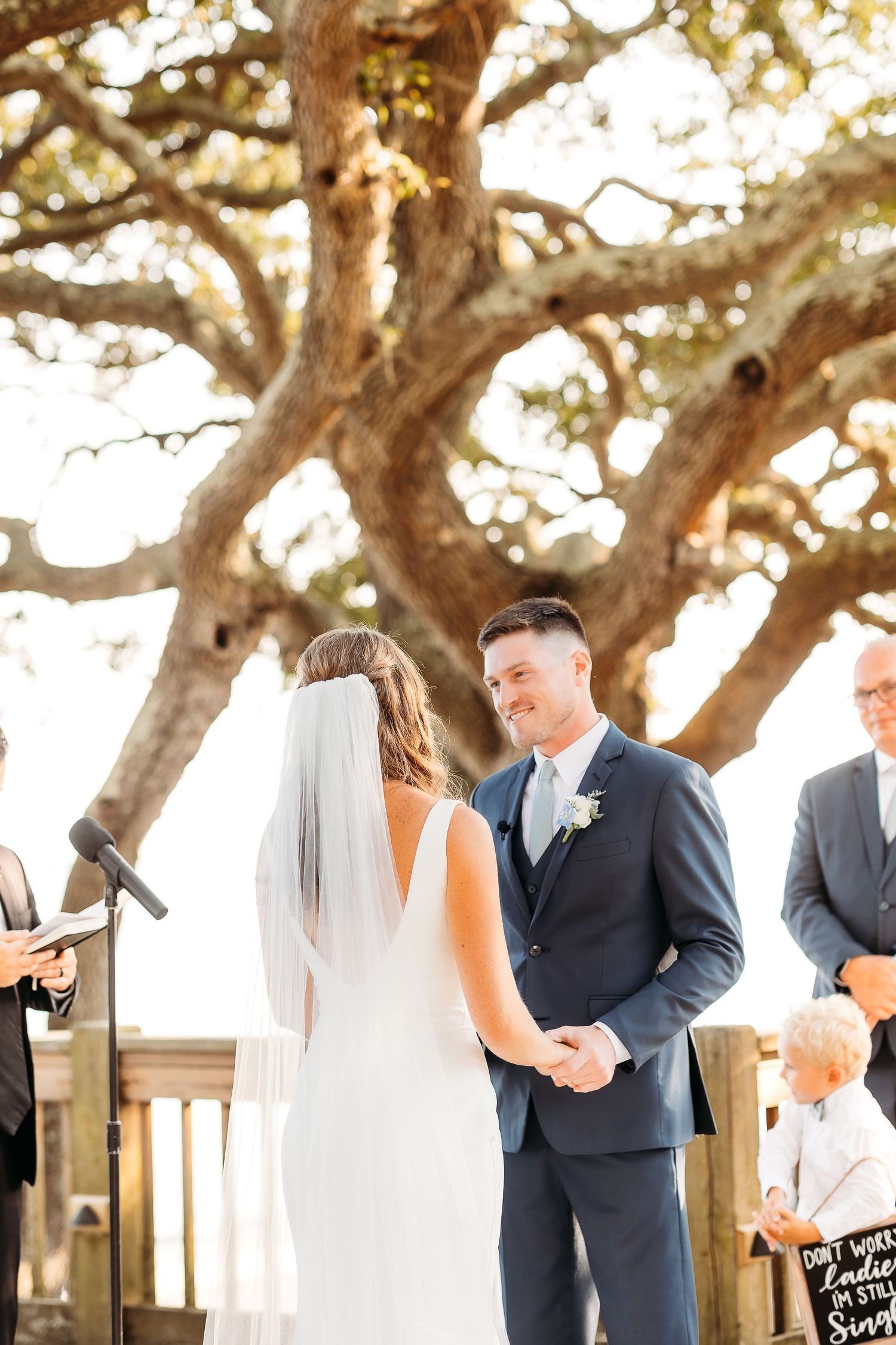 A couple shares an intimate first look moment under large oak trees at an outdoor wedding ceremony.