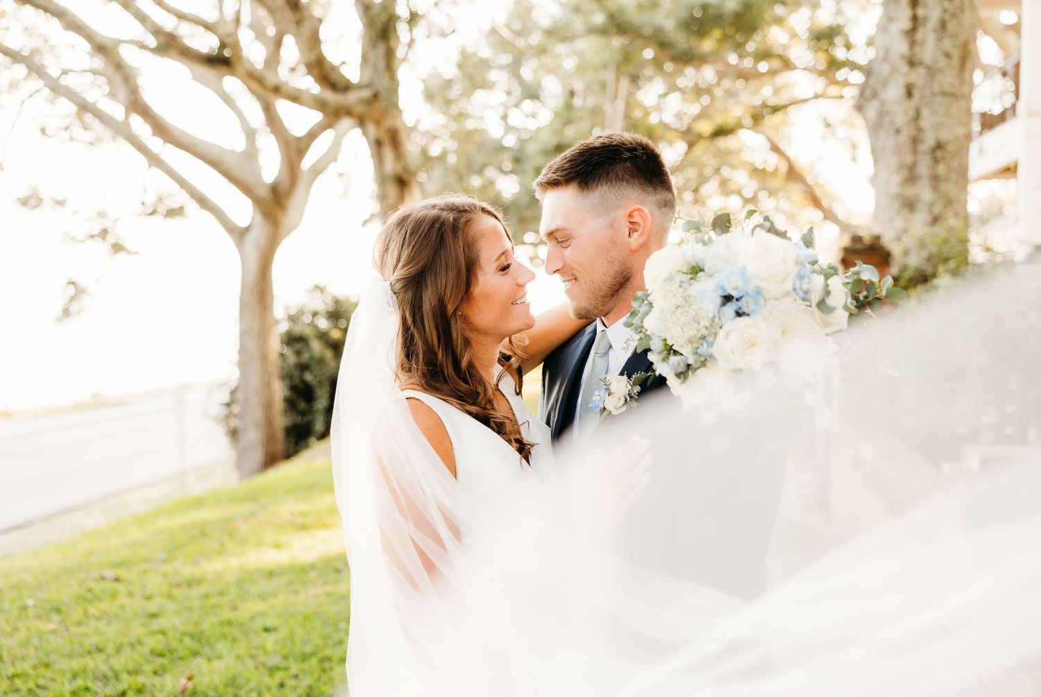 A couple shares a romantic moment together in a sunlit outdoor setting with trees in the background.