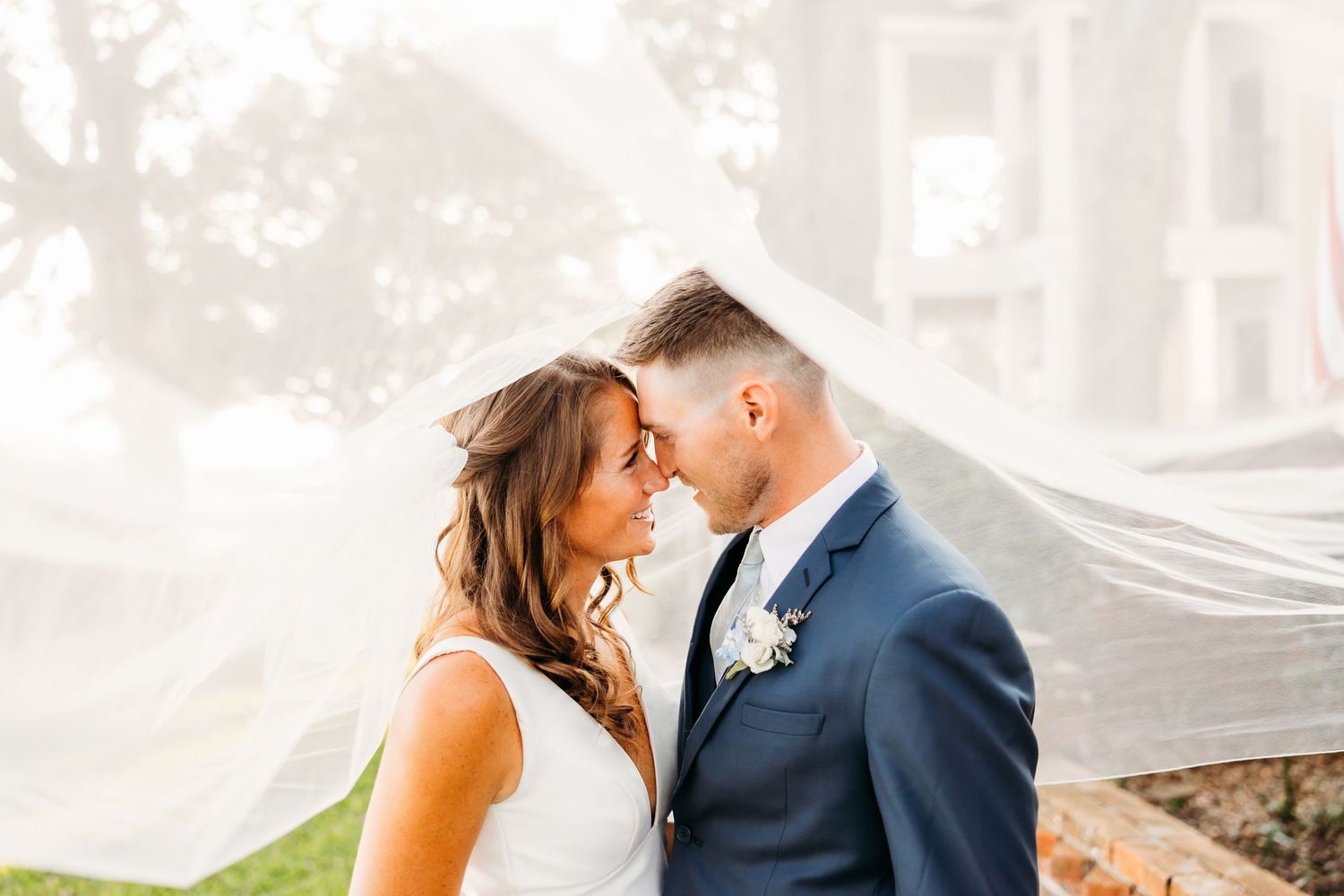 A romantic couple shares a tender kiss outdoors with soft lighting and elegant wedding attire.