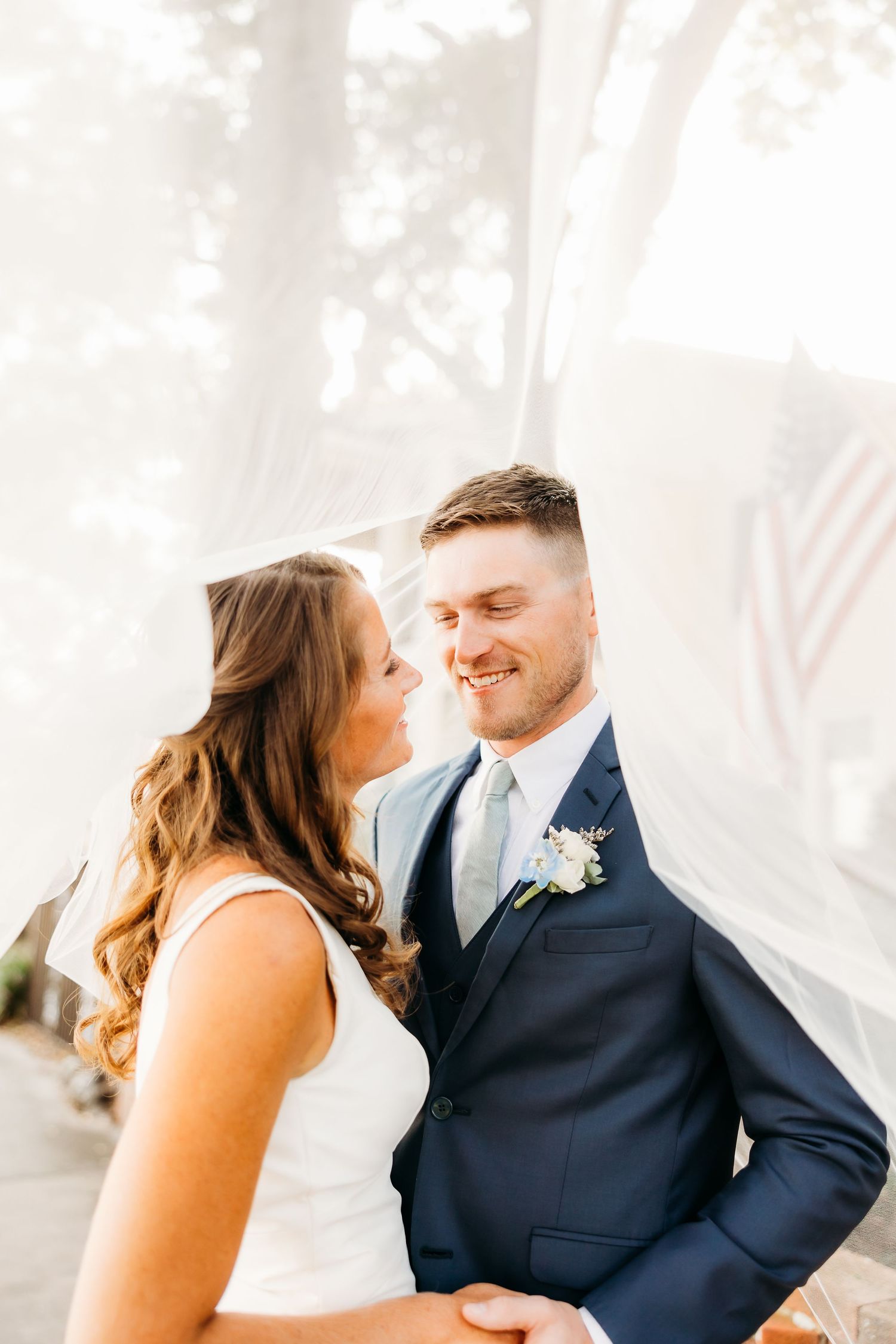 Romantic wedding couple sharing intimate moments in a bright, sunlit setting with white curtains.