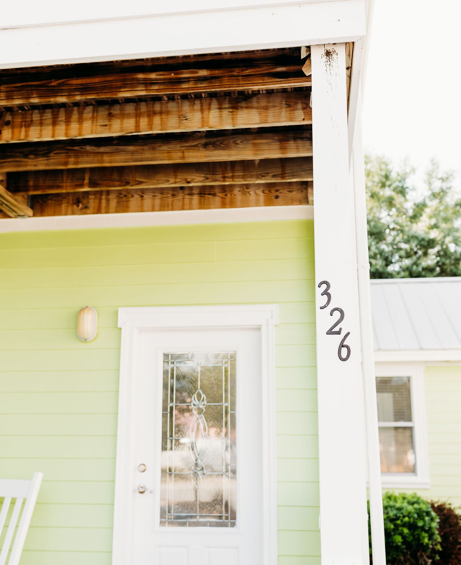 A mint green house exterior with white trim and wooden beams visible under the porch overhang.