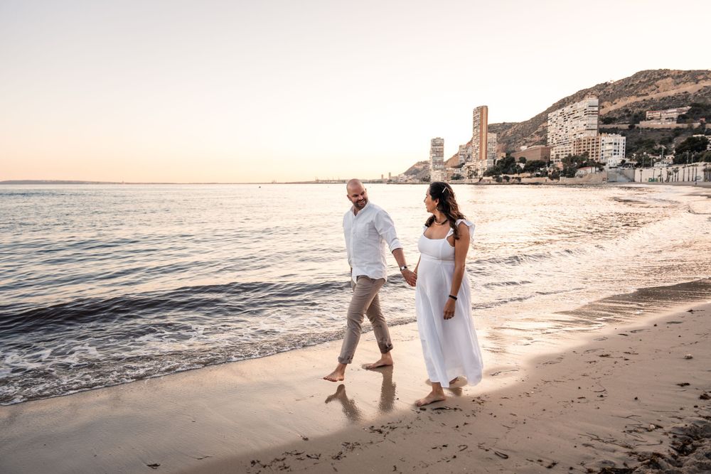 Couple holding hands and walking along the beach at sunset for a Maternity photo shoot in Alicante Spain