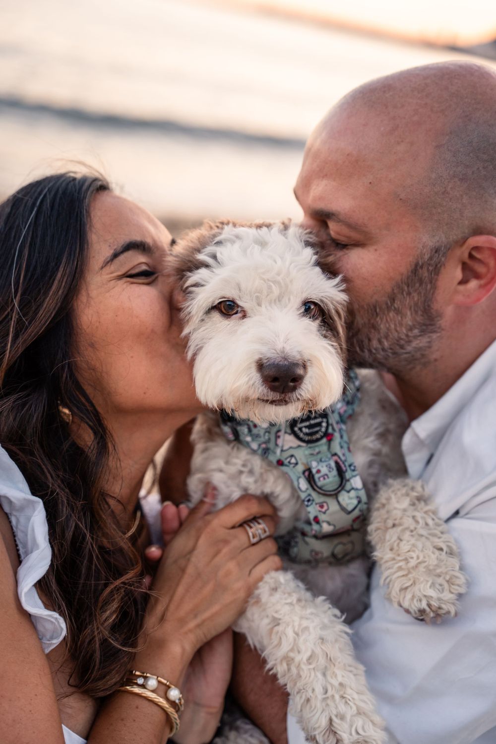 Couple kissing their dog and dog looking at camera while they are at the beach at sunset in Alicante