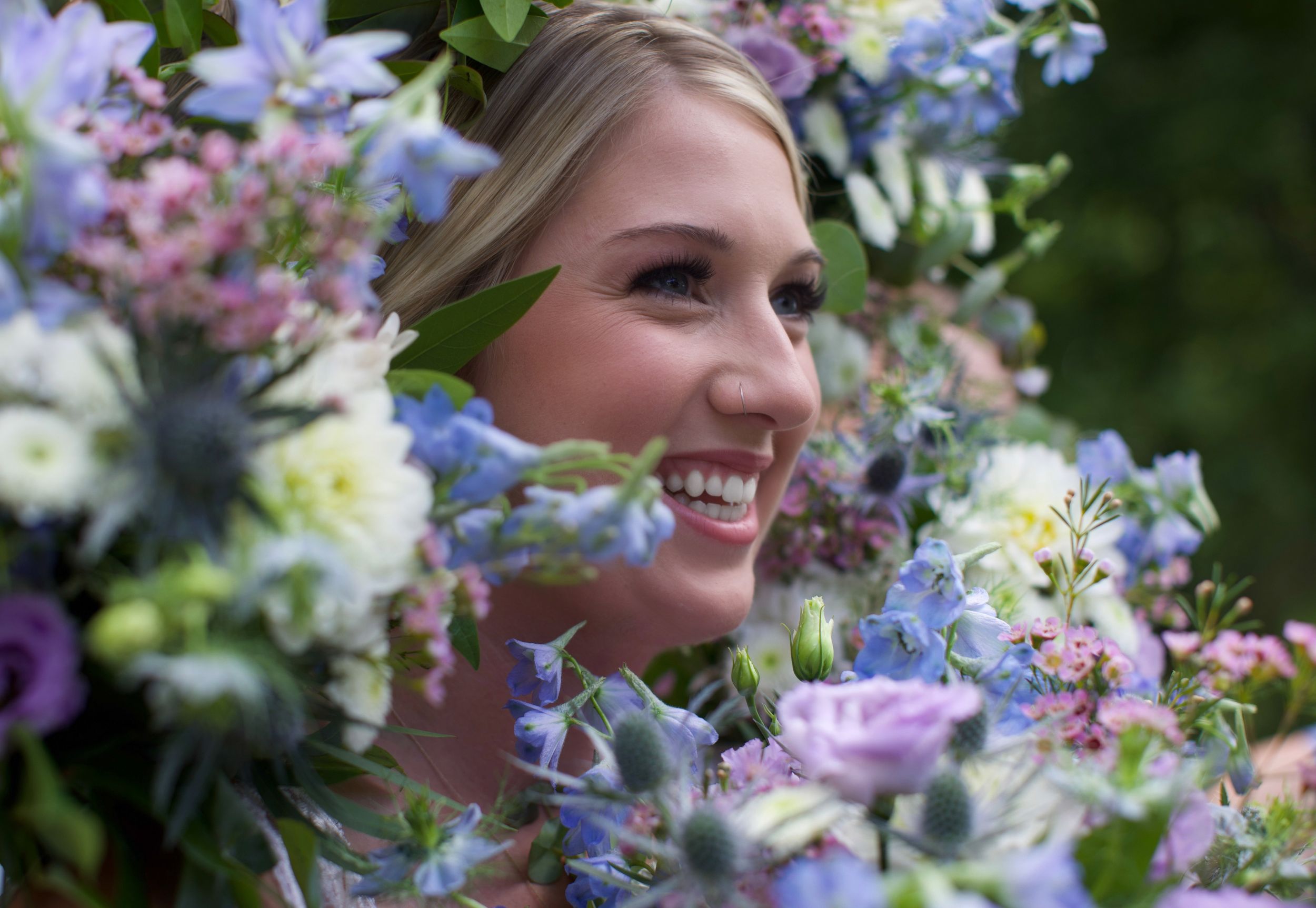 Delicate bouquet of purple and blue flowers with white blooms sitting against a natural outdoor background.