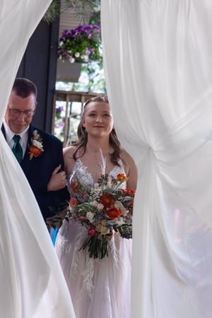 Wedding entrance through white curtains with bride holding autumn-colored bouquet.