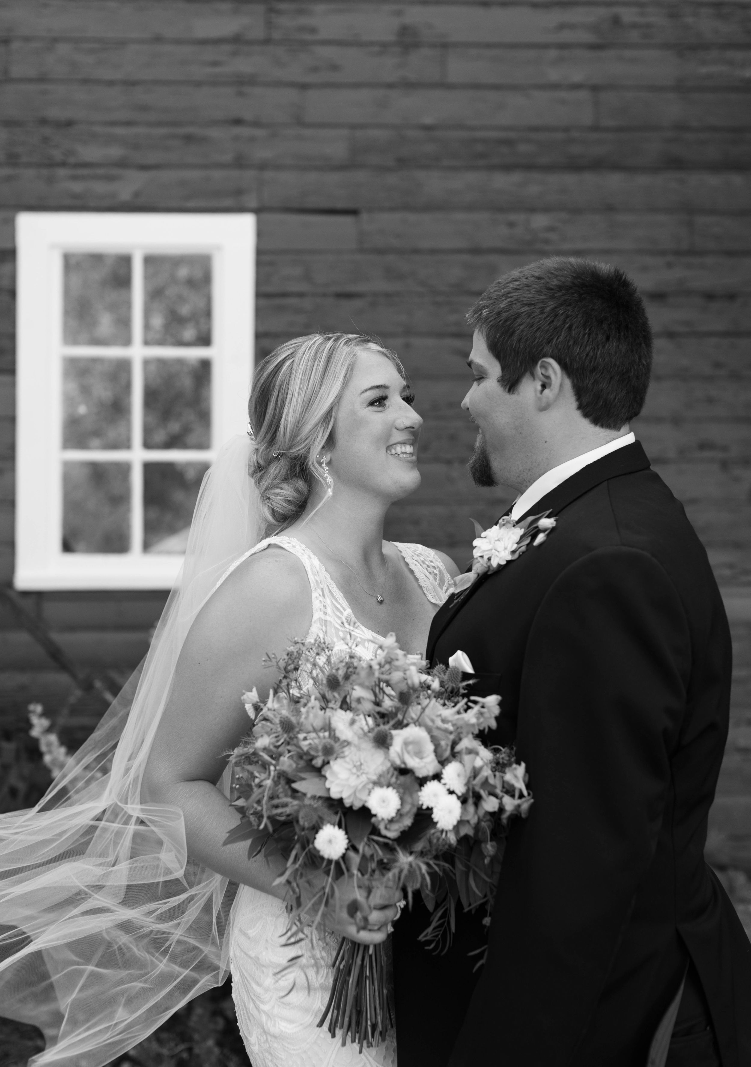 Black and white wedding portraits showing tender moments between newlyweds against a rustic wooden wall.