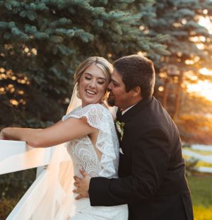 Romantic sunset portrait of newlyweds with flowing veil against evergreen trees.